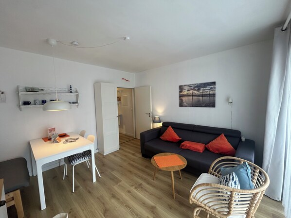 Een moderne woonkamer met een witte tafel, een zwarte bank en een rieten stoel.