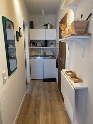 A compact kitchen with white cabinets, a microwave, a kettle, and a sink. - Lüttjer Kiwitt - perfect location for short distances and relaxing days (Wangerooge)