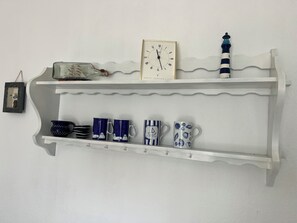 Une étagère blanche ornée d’objets décoratifs, notamment une horloge, une maquette de phare et diverses tasses en céramique.