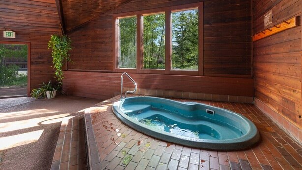 A wooden cabin with a hot tub, a window with a view of trees, and an exit sign. - Silverthorn Skiing & Hiking with Community pool/hot tub/Sauna. (Silverthorne)