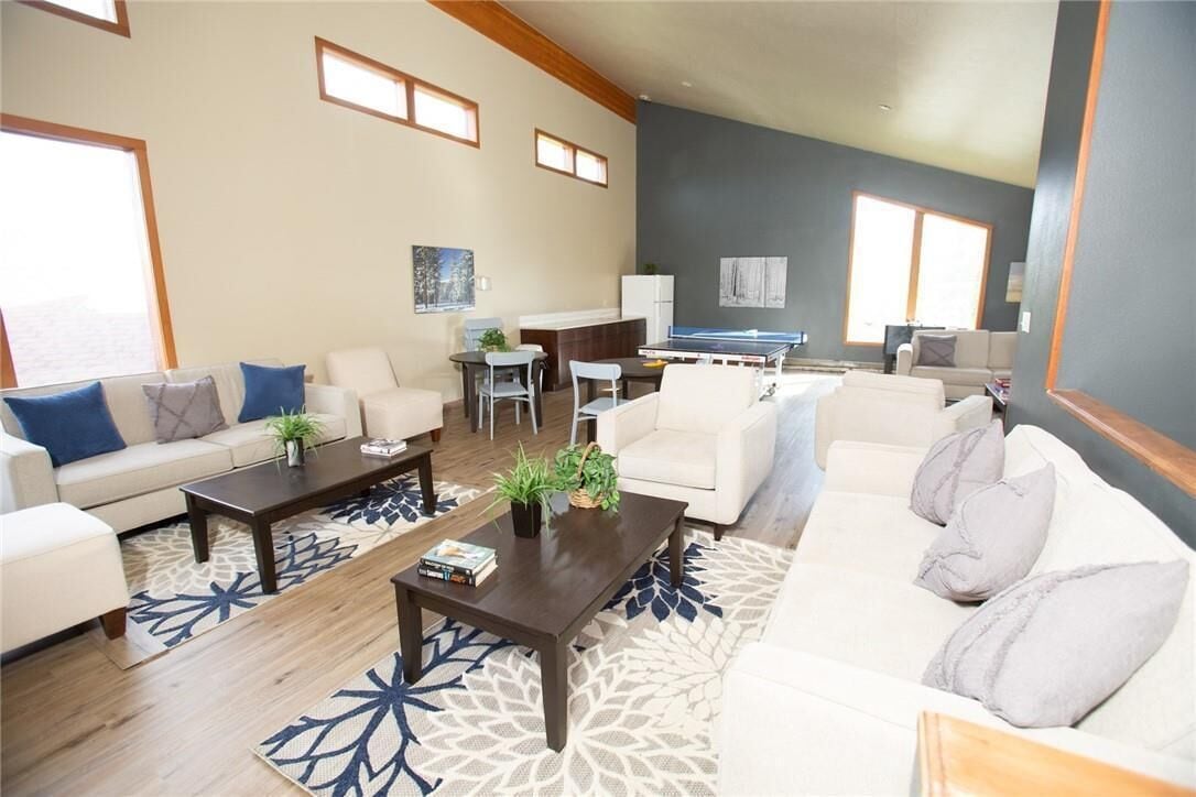 A spacious living room with a sofa, coffee table, and a ping pong table. There is a dining area with a table and chairs, and a kitchen area with a refrigerator.