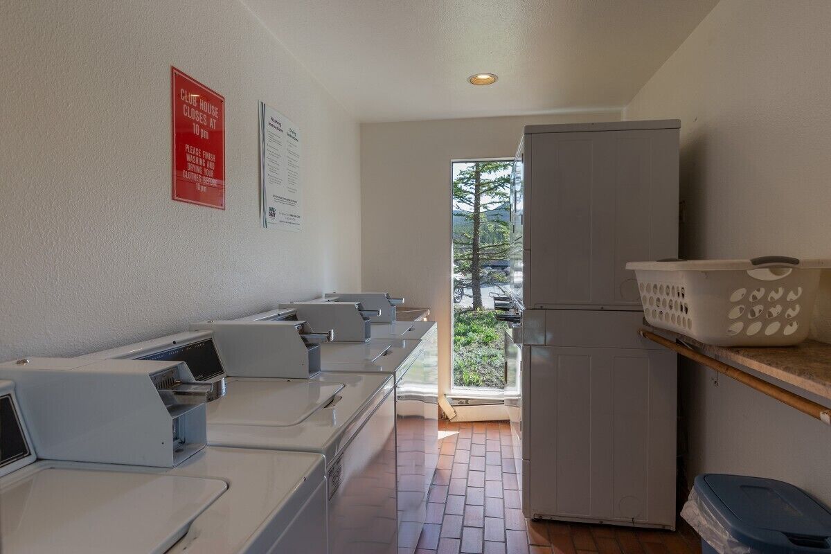 A laundry room with multiple washing machines, a refrigerator, and a basket on a shelf.