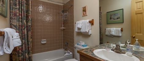 Uma casa de banho com banheira, sanita e lavatório. Há toalhas penduradas na parede e um separador de chuveiro.