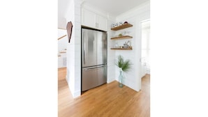 A modern kitchen with white cabinets, a stainless steel refrigerator, wooden flooring, and a small potted plant. - The Robin house - Close to Everything! (Mount Pleasant)