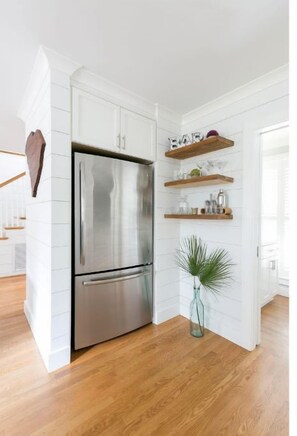 Una cocina moderna con armarios blancos, un refrigerador de acero inoxidable, piso de madera y una pequeña planta en maceta.
