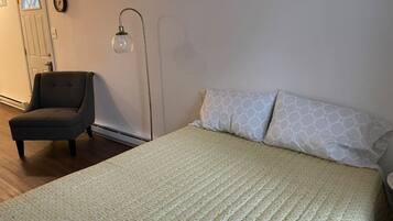 A bedroom with a bed, a chair, a floor lamp, and a door.