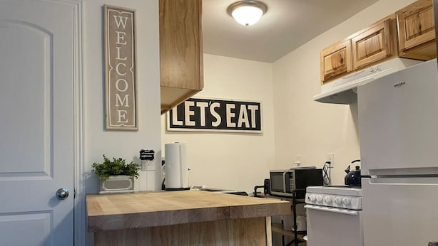 Une cuisine compacte avec un îlot central en bois, des appareils électroménagers blancs et deux panneaux décoratifs au mur.