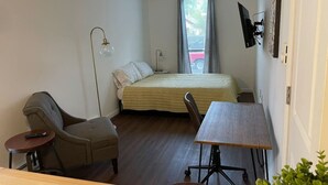 Une petite pièce bien éclairée, avec un lit, un bureau, une chaise et une lampe.