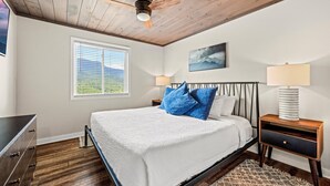 A bedroom with a bed, wooden ceiling, window, wall art, bedside lamps, and a dresser. - Mountain-View Condo w/ Pool & Hot Tub Access (Gatlinburg)