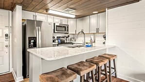 A modern kitchen with white cabinets, stainless steel appliances, a marble countertop, and wooden stools. - Mountain-View Condo w/ Pool & Hot Tub Access (Gatlinburg)