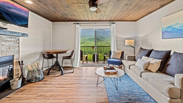 A cozy living room with a fireplace, a sofa, a coffee table, and a balcony with a view. - Mountain-View Condo w/ Pool & Hot Tub Access (Gatlinburg)