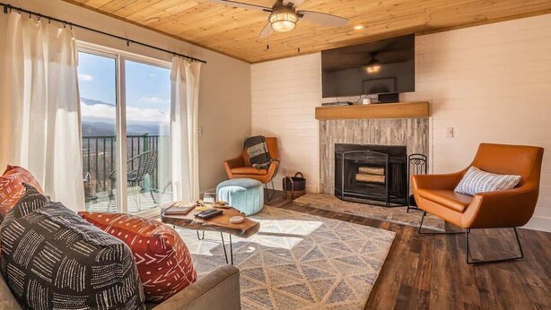 Una sala de estar acogedora con chimenea, ventilador de techo y vistas al exterior.