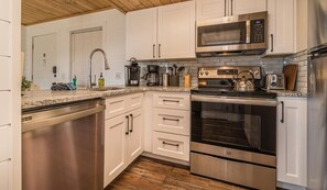 A modern kitchen with stainless steel appliances, white cabinetry, and a wooden floor.