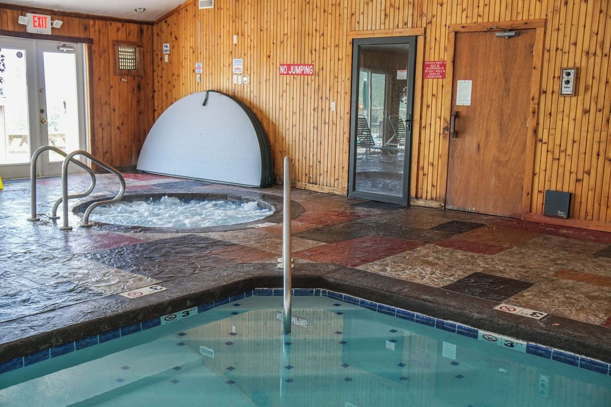 Een binnenzwembad met een jacuzzi, houten wanden en een betegelde vloer.