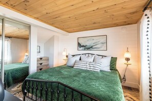 Un dormitorio con techo de madera, una cama con ropa de cama verde, dos lámparas de noche y un cuadro en la pared.