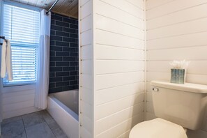 Un baño con bañera, inodoro y ventana con persianas.