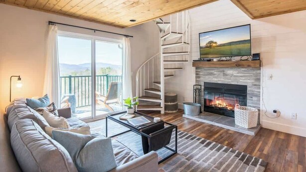 Ein modernes Wohnzimmer mit Kamin, einer Wendeltreppe und einem großen Fenster mit herrlicher Aussicht.