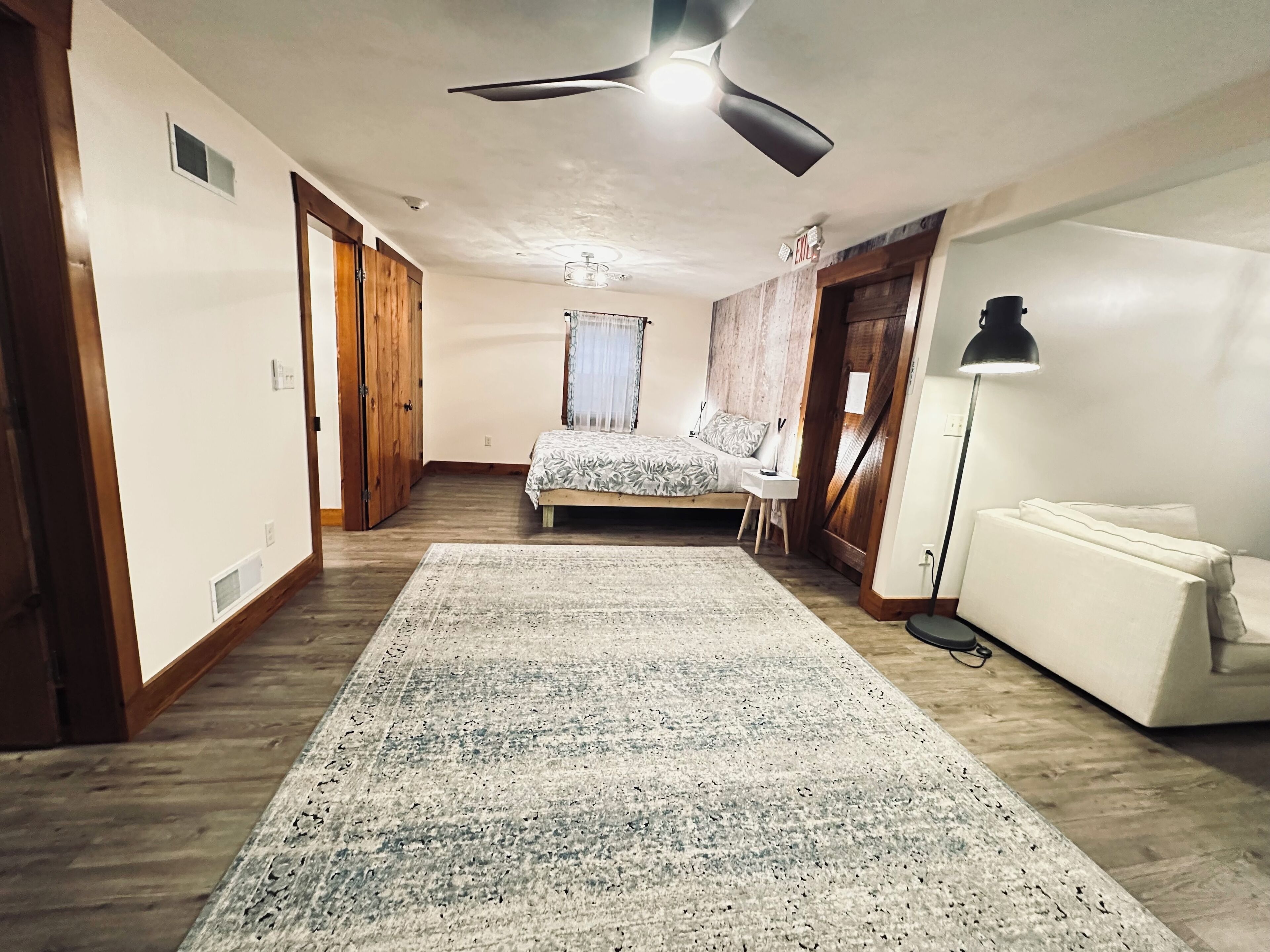 Een slaapkamer met een bed, een staande lamp, een vloerlamp, een plafondventilator en een groot tapijt.