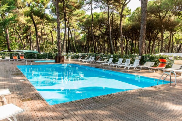 A rectangular swimming pool with a wooden deck surrounding it, lined with white and orange lounge chairs. - Club Del Sole Marina Romea Easy Camping Village (Ravenna)