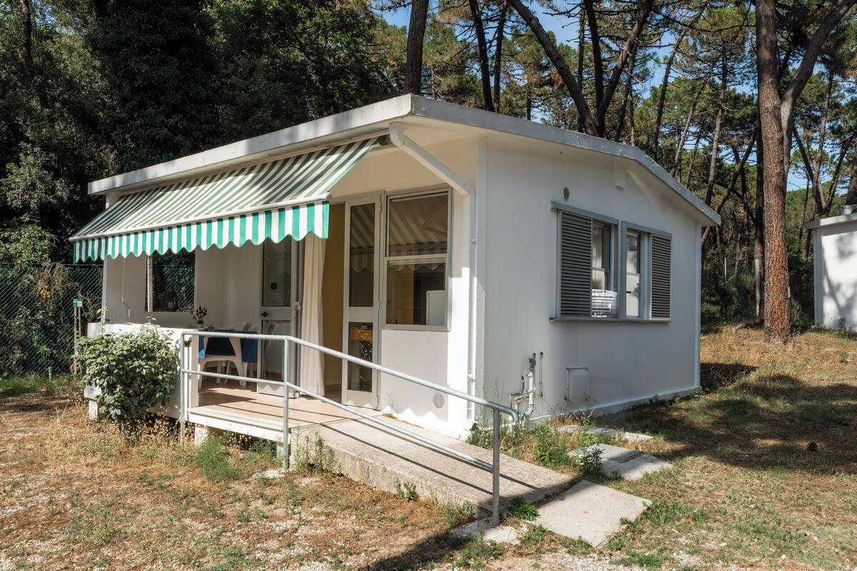 A small, single-story cabin with a covered porch, a small outdoor seating area, and a staircase leading to the entrance.