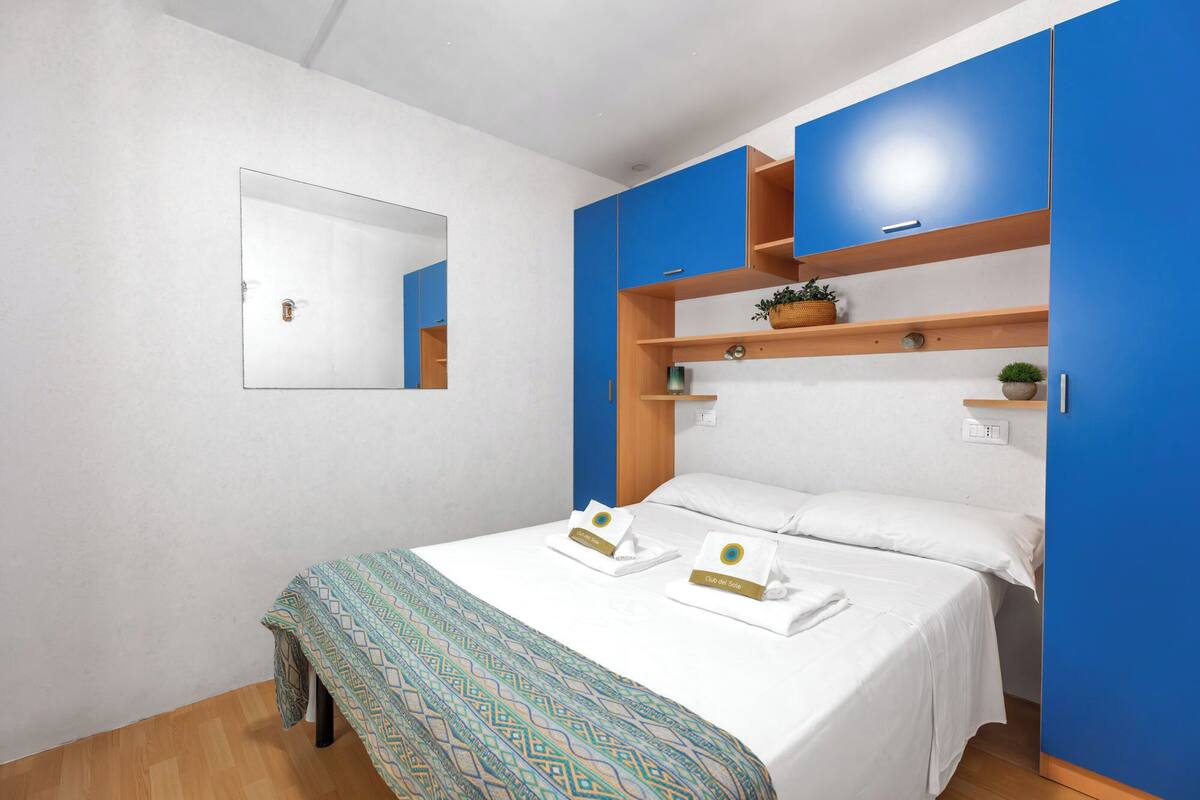 A bedroom with a bed, two bedside tables, a mirror, and blue cabinets.