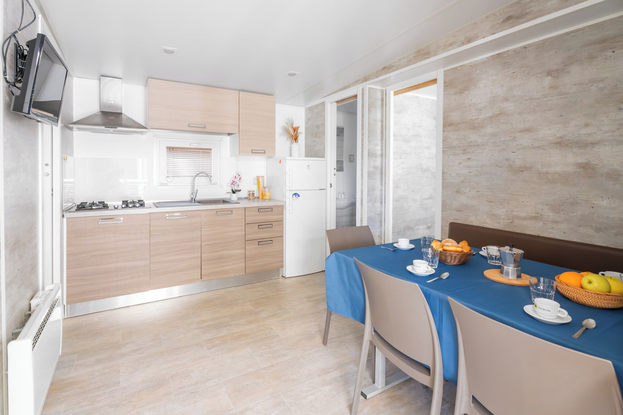 A modern kitchen with a dining area, featuring a built-in oven, a refrigerator, and a dining table set with breakfast items.
