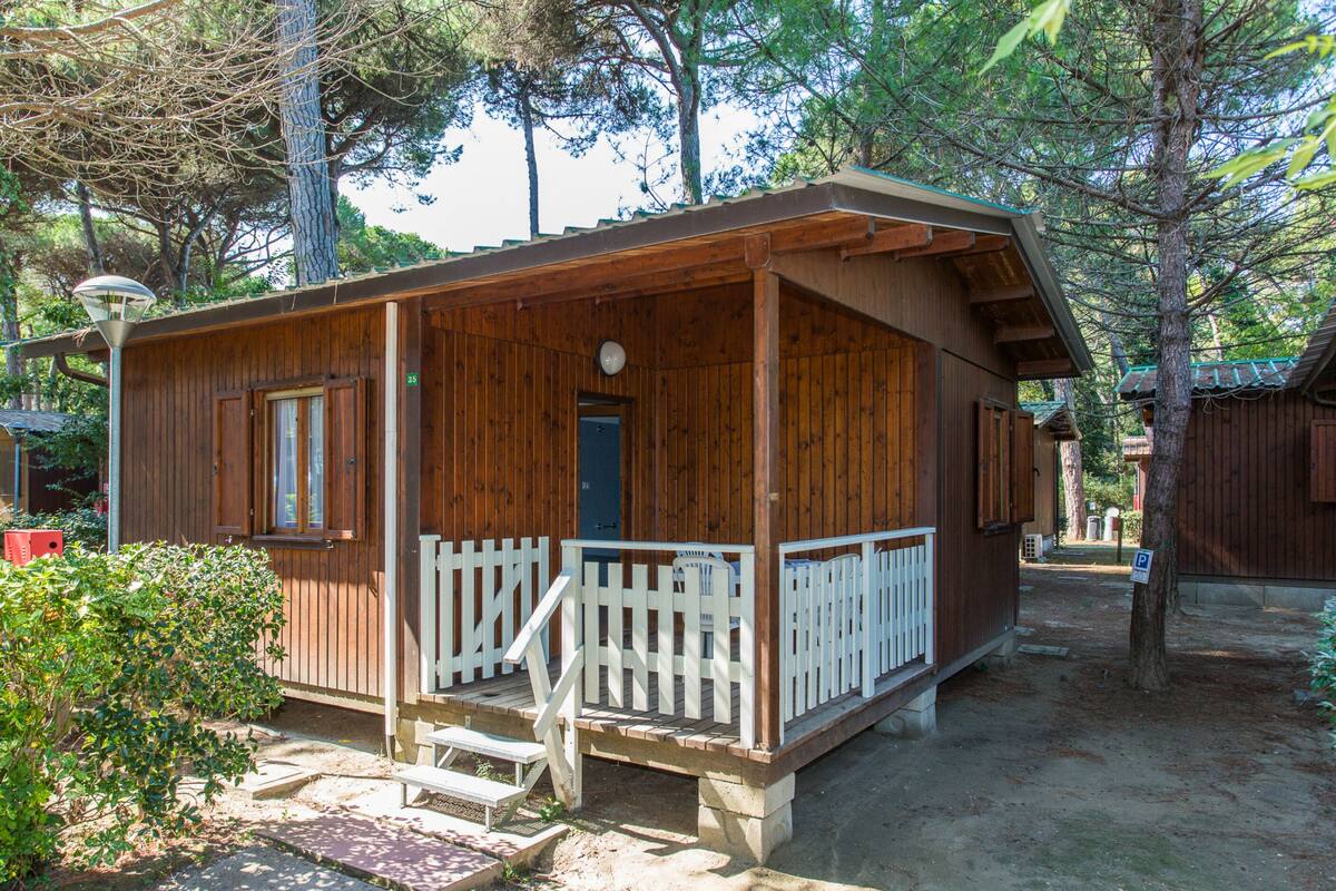 A small wooden cabin with a porch and a door, surrounded by trees.