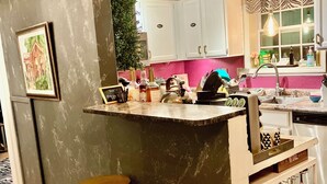 Cuina amb armaris blancs, un respatller rosa i una zona de bar amb tamborets.
