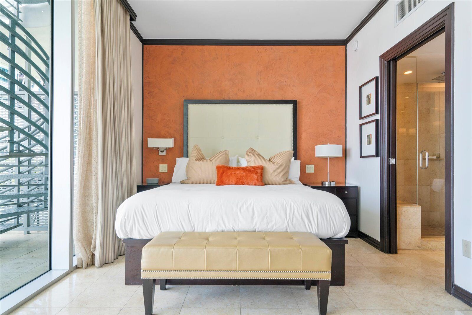 Een moderne hotelkamer met een groot bed, een bankje en uitzicht op de stad.