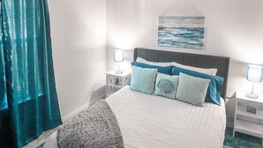 Una camera d'albergo con un letto, due comodini con lampade, un quadro appeso al muro e una tenda.