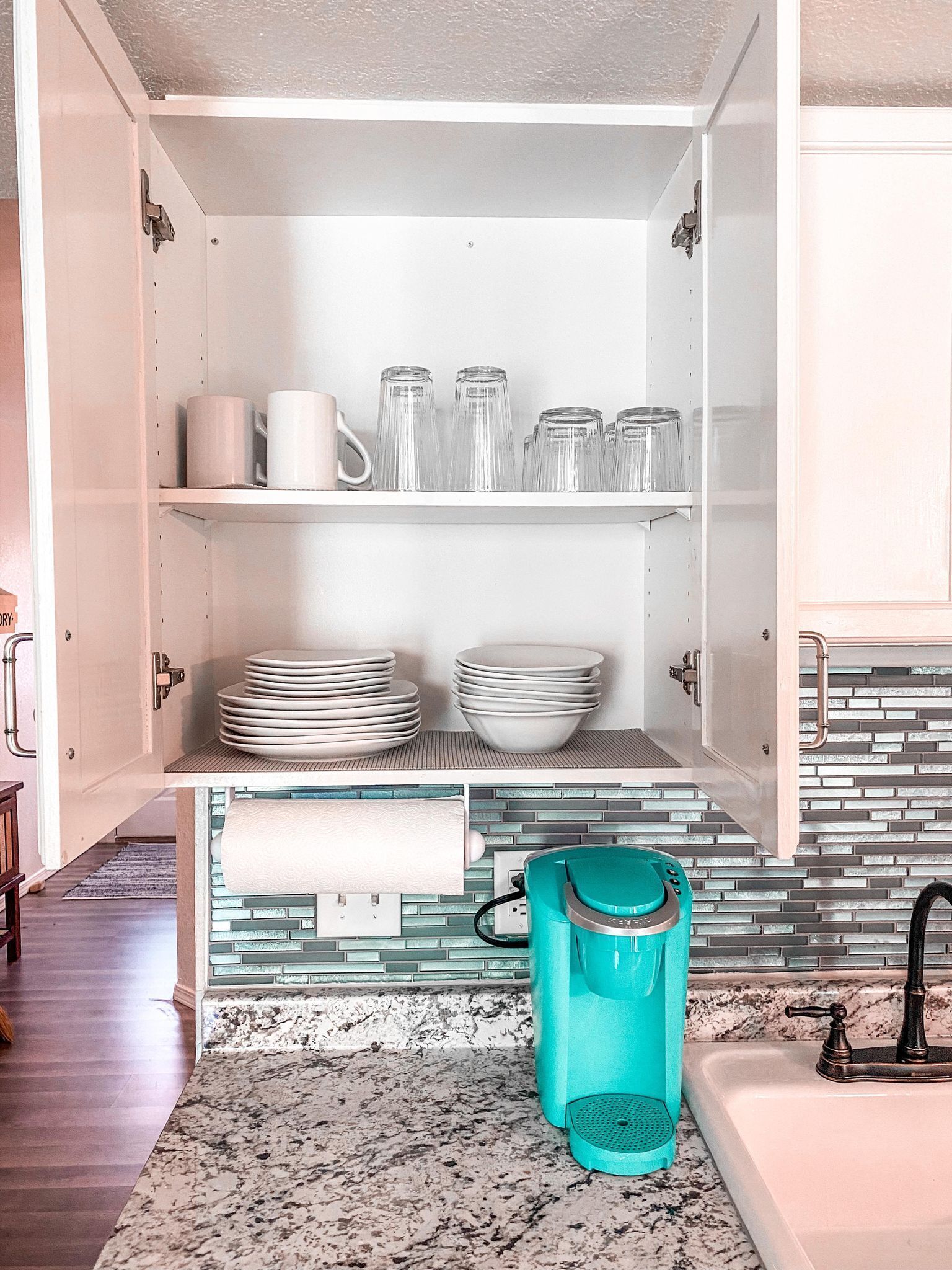 A kitchen with white cabinets, a tiled backsplash, and a teal trash can.