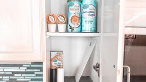 Una cucina con un armadietto bianco che contiene diversi alimenti, un lavello e uno schienale rivestito di piastrelle blu.