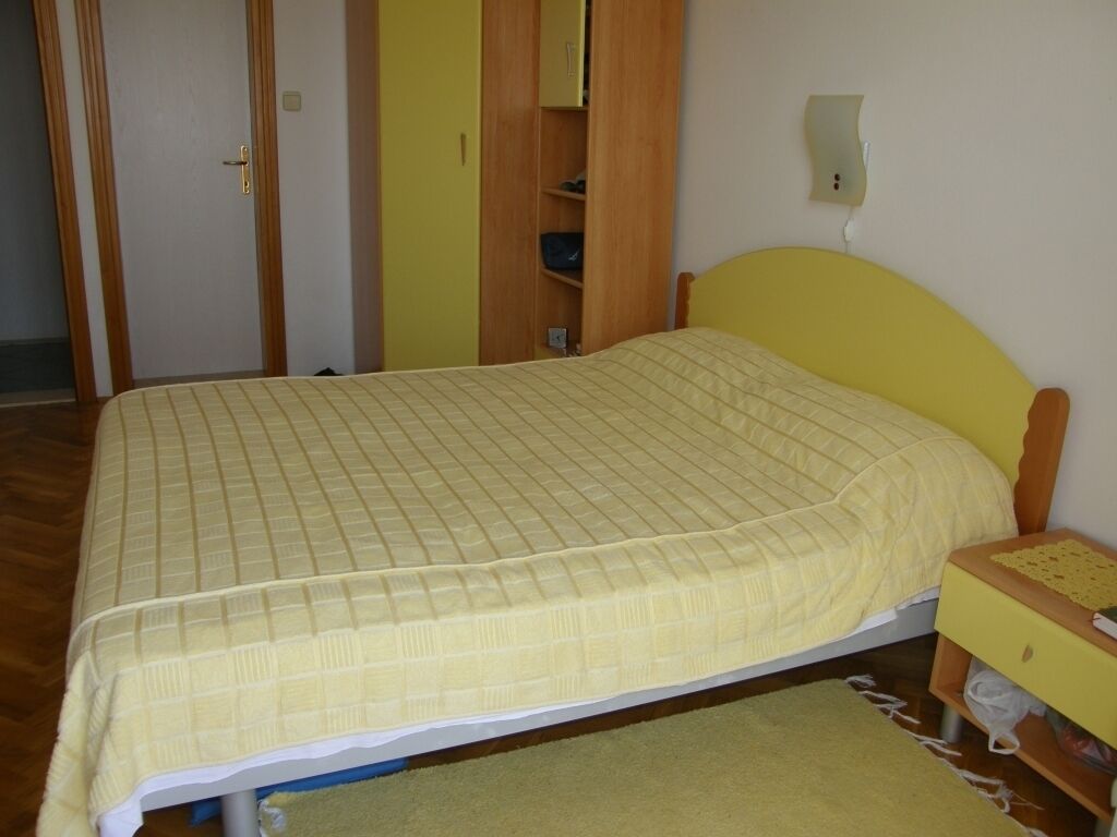 A bedroom with a bed, a wooden wardrobe, and a bedside table.