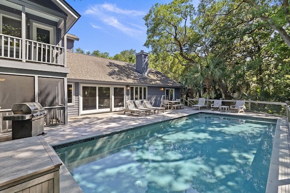 Une piscine avec une terrasse, des chaises longues et un barbecue.