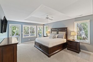 Une chambre à coucher avec un grand lit, deux tables de chevet, un ventilateur de plafond et des fenêtres équipées de stores.