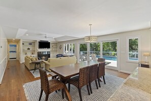 Un vaste salon doté d’une cheminée, un coin repas avec une grande table et des chaises, et une vue sur la piscine grâce à de grandes portes coulissantes.