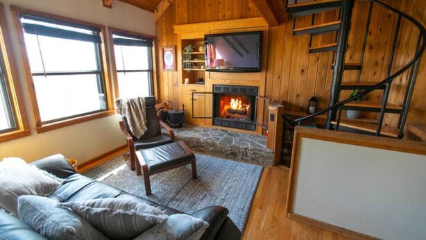 Una sala de estar acogedora con chimenea de piedra, un sofá cómodo, una silla de madera y un televisor sobre la chimenea.