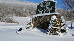 Señal de Black Bear Resort con un arco de piedra y árboles cubiertos de nieve al fondo.