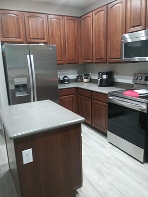 A kitchen with wooden cabinets, stainless steel appliances including a refrigerator, microwave, and oven, and a built-in water dispenser.