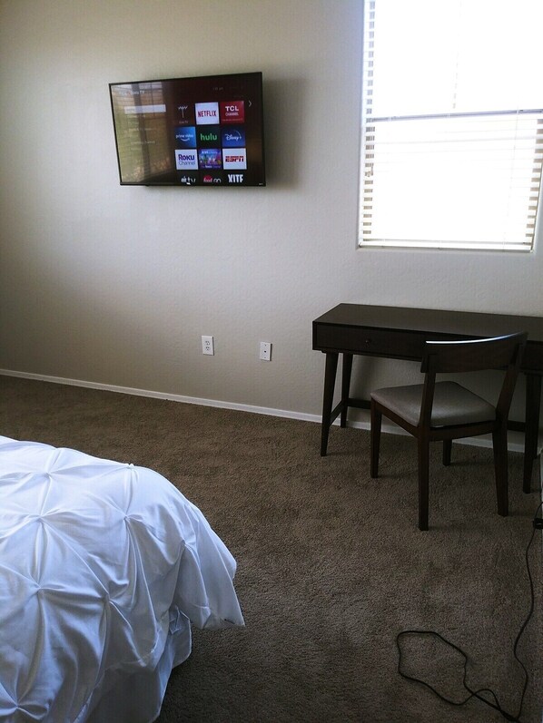 A bedroom with a bed, a desk, and a TV mounted on the wall displaying various streaming services.