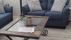 A living room with a blue sofa, a glass coffee table with a patterned mug, a framed picture on the wall, and a floor lamp. - VILLA Verde Surprise Stadium - Resort Living (Surprise)