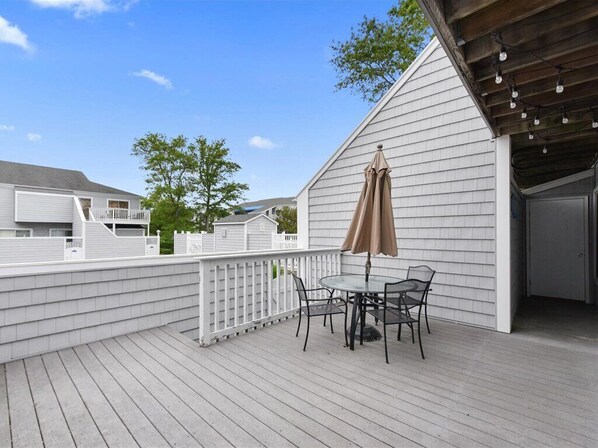 Eine Holzterrasse mit Tisch und Stühlen, ein mit Lichtern versehener Pergola und ein weißer Zaun.
