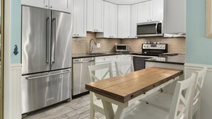 A modern kitchen with white cabinets, stainless steel appliances, and a wooden dining table. - 2 BR 2 BA Unit W/Pool and Close to Northside Park (Ocean City)