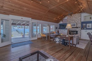 A cozy cabin interior with a wooden ceiling, a dining area, a fireplace, and a view of the water outside. - The Crab Shack on Carter's Creek (Weems)