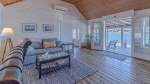 Ein geräumiges Wohnzimmer mit hohen Decken, einer Couch, einem Couchtisch und Blick auf das Wasser durch große Schiebetüren.