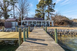 Waterfront property with a dock, shed, and outdoor seating area surrounded by natural surroundings and a rocky shoreline.