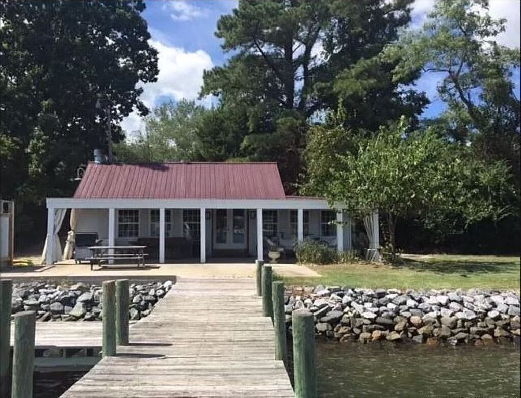 A wooden dock leading to a building with a red roof, surrounded by trees and a body of water.
