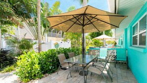 An outdoor patio with a table and chairs, a large umbrella, and lush greenery. - Seaglass Inn at the Beach Shack  Just one block from the beach! (Englewood)