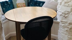 A round wooden table with a black chair in front, set against a white wall with a textured stone feature. - Fisherman's Cottage, a haven in Padstow old town (Padstow)