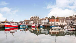 A harbor with several boats docked, a variety of buildings, and a calm water surface reflecting the structures. - Fisherman's Cottage, a haven in Padstow old town (Padstow)